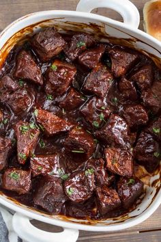 a white bowl filled with cooked beef and garnished with parsley on top