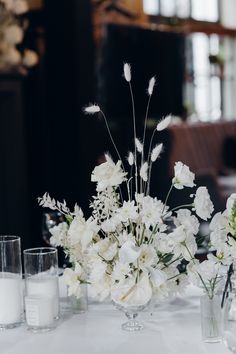 white flowers in vases sitting on a table with candles and glasses next to them