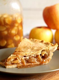 a piece of pie on a plate next to apples