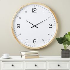 a clock on the wall above a white dresser with books and a potted plant