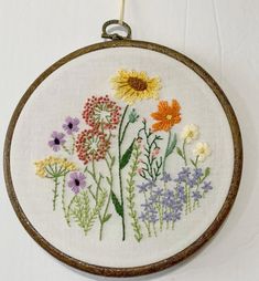 a white wall hanging with flowers on it and a wooden frame holding the embroidery work