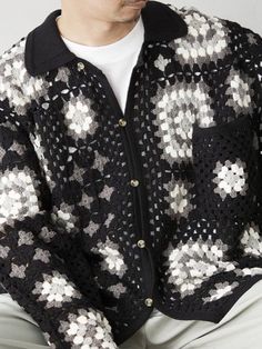 a man sitting down wearing a black and white sweater with silver stars on the sleeves