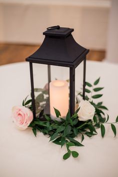 a candle is lit on top of a table with flowers and greenery around it