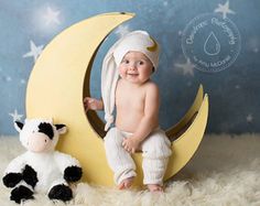 a baby sitting on the moon next to a stuffed cow