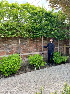 a man standing in front of a brick wall with green plants growing on the side