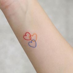 two hearts tattoo on the wrist with colors painted on each arm and behind it is an orange, blue, and red heart