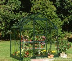 a small green house sitting in the middle of a yard filled with flowers and plants