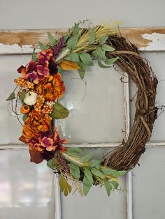 a wreath is hanging on the wall with flowers and leaves in front of an old window