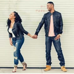 a man and woman holding hands while standing next to a wall