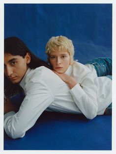 two people laying on the ground with their arms around each other and one person looking at the camera