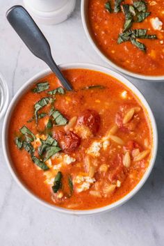 two bowls of tomato soup with basil on top