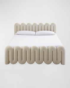 an upholstered bed with white sheets and pillows