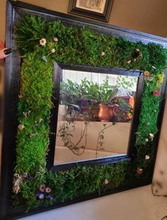 a mirror that is covered in plants and flowers on the wall next to a potted plant