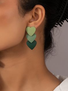 a close up of a person wearing green and black heart shaped earrings on their ears