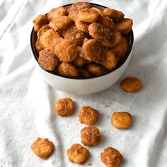 a bowl filled with fried food sitting on top of a white cloth next to a pile of doughnuts