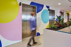 a man walking through an office lobby with colorful walls and planters on the wall