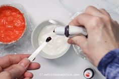 someone is painting something red on a white bowl with an orange substance in the background