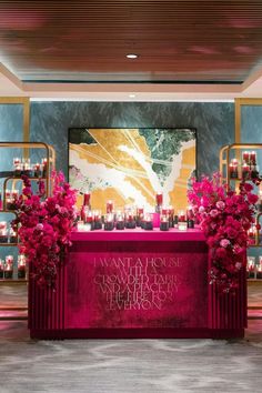 a red table with candles and flowers on it in front of a wall full of pictures