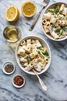 two bowls filled with pasta next to lemons and seasonings on a marble table