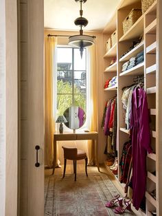 an open closet with clothes and shoes on the shelves, next to a table in front of a window