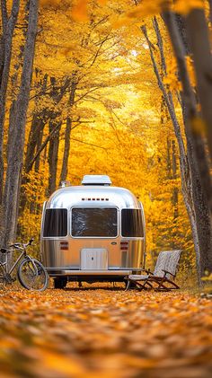 an airstream parked in the woods with autumn leaves on the ground and a bicycle leaning against it