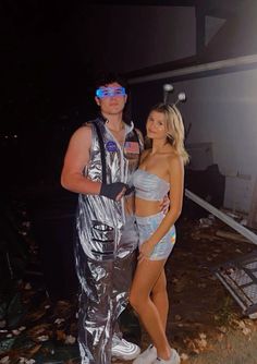 a man and woman dressed up in costumes standing next to each other outside at night