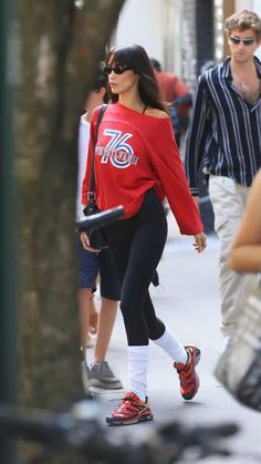 a woman in red shirt and black leggings walking down street with other people