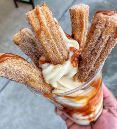 a hand holding a glass filled with desserts on top of a sidewalk next to a table