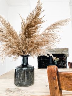 a vase filled with dry grass sitting on top of a table next to a wooden chair