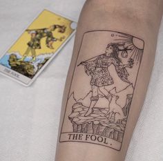 a tattoo on the arm of a person with a tarot card in front of them