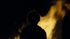 a person standing in front of a fire with their back turned to the camera, at night