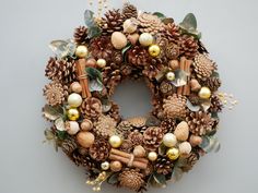 a wreath with pine cones and ornaments hanging on the wall next to a gray wall