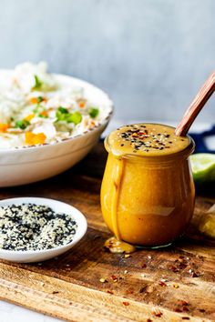 a wooden cutting board topped with a bowl of food and a jar filled with rice