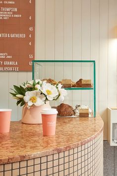 there are three cups on the counter at this coffee shop with flowers in front of them