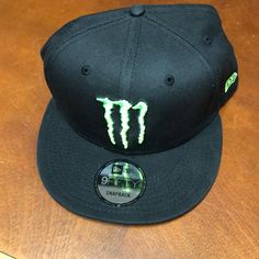 a black hat with neon green monster logo on the front and back side, sitting on top of a wooden table