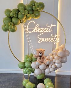 a teddy bear sitting on top of balloons in front of a sign