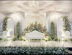 a white couch sitting under a chandelier covered in flowers and greenery next to chairs