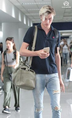 a young man is looking at his cell phone while walking through an airport terminal with other people in the background