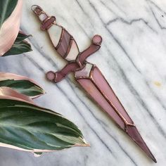 a pink stained glass cross on a white marble table next to a green leafy plant