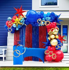 an arch decorated with balloons and streamers in front of a blue house on a sunny day