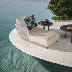 a couch and table sitting on top of a white surfboard next to the ocean