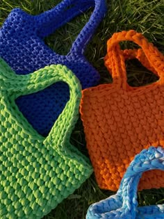 three knitted handbags laying on the ground in green, blue, and orange