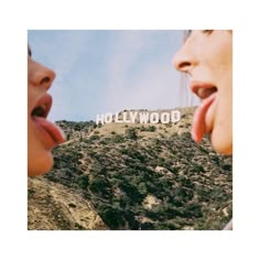 two people sticking their tongues out in front of the hollywood sign