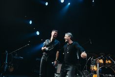 two men standing next to each other in front of microphones and drums on stage