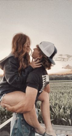 a man holding a woman on his back in front of a cornfield at sunset