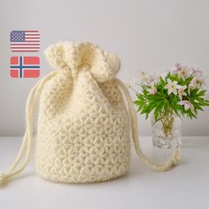 a crocheted bag next to a vase with flowers