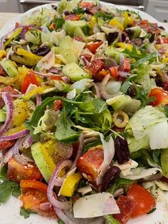 a large salad on a white plate with tomatoes, onions, lettuce and olives