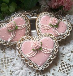 three heart shaped cookies decorated with pink icing on a lace doily next to flowers