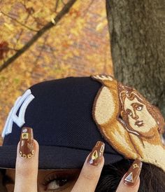 a woman with her hands on her head and nails painted gold, wearing a baseball cap