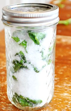 a glass jar filled with green leaves on top of a wooden table